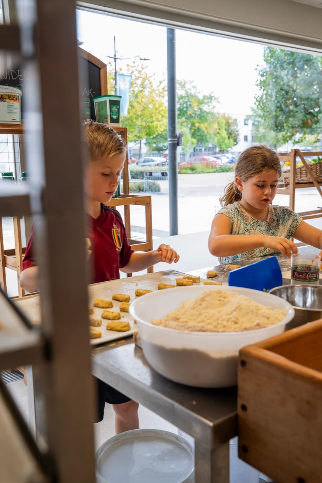 Twee kinderen kneden deeg aan de werktafel bij het raam.