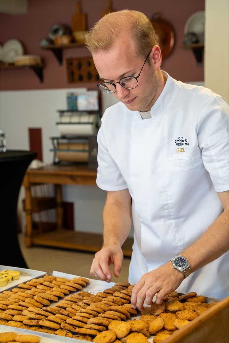 Giel Creemers legt koekjes op plateaus in het atelier.